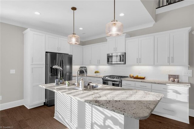 kitchen with appliances with stainless steel finishes, a center island with sink, white cabinets, and decorative light fixtures