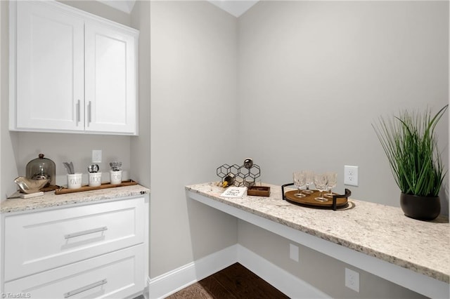 bar featuring white cabinetry, wood-type flooring, light stone countertops, and built in desk