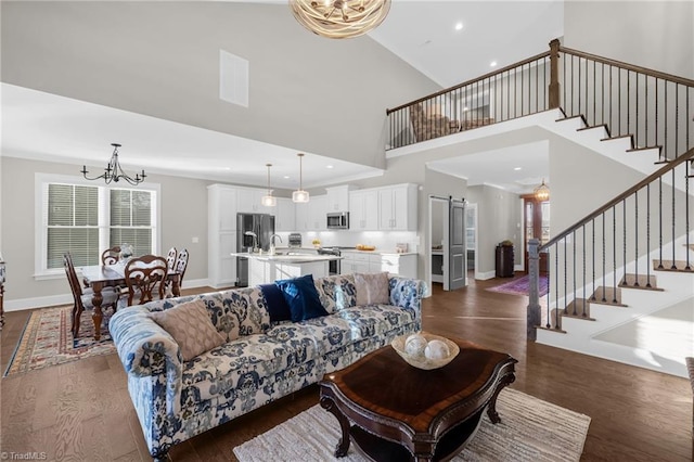 living room with dark hardwood / wood-style floors, sink, a high ceiling, a barn door, and an inviting chandelier