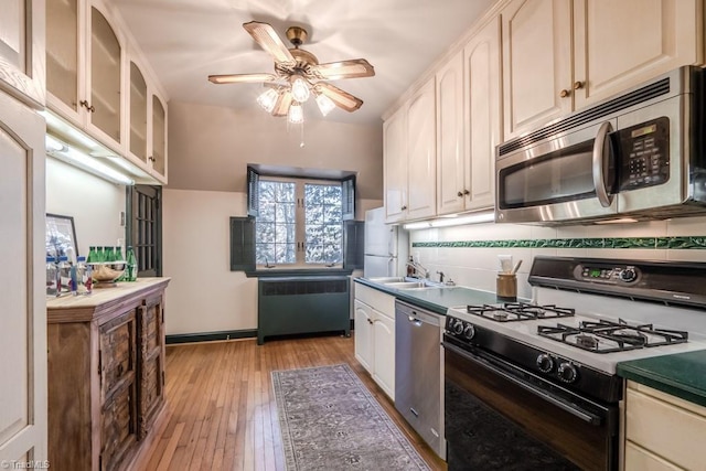 kitchen with ceiling fan, radiator heating unit, stainless steel appliances, tasteful backsplash, and light hardwood / wood-style floors