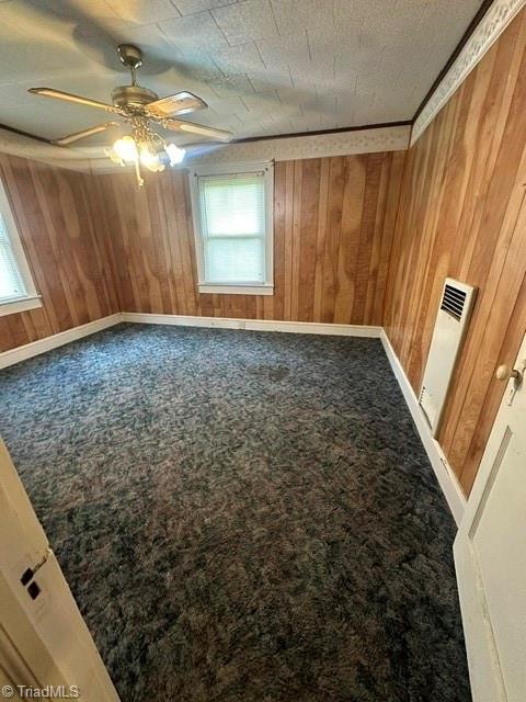 carpeted empty room with wooden walls, ceiling fan, and radiator