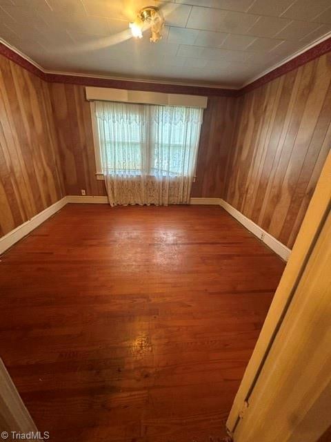 spare room featuring dark hardwood / wood-style floors, ornamental molding, and wood walls