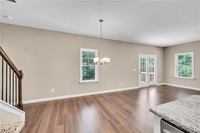 unfurnished dining area with wood finished floors, a chandelier, baseboards, and stairs