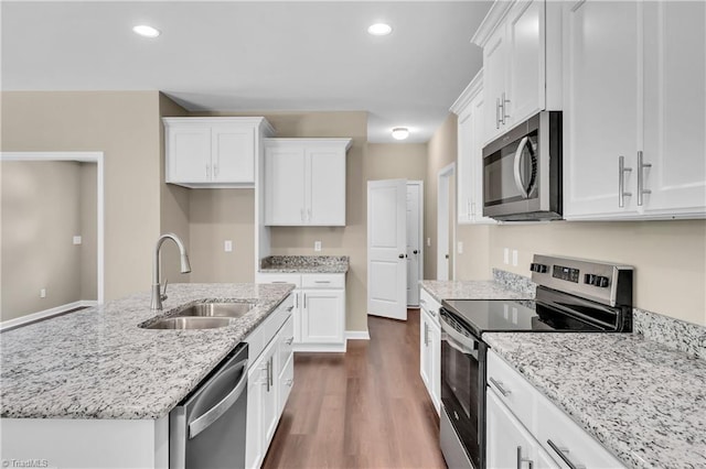 kitchen with stainless steel appliances, a sink, white cabinetry, dark wood-style floors, and light stone countertops