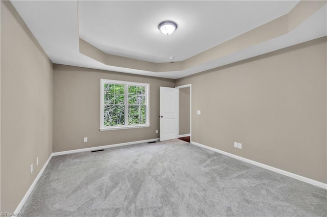 carpeted empty room with a tray ceiling and baseboards