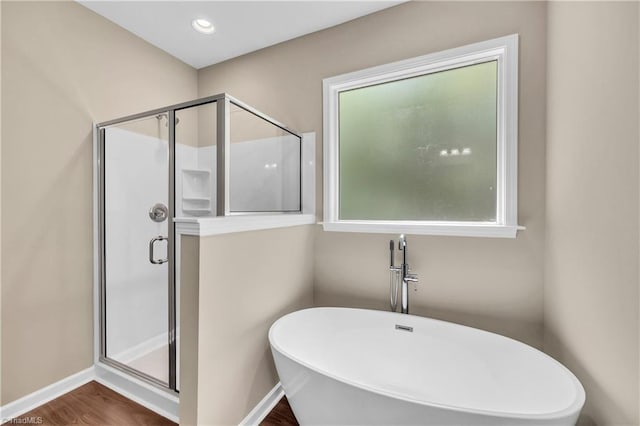 bathroom with a shower stall, a freestanding bath, wood finished floors, and baseboards