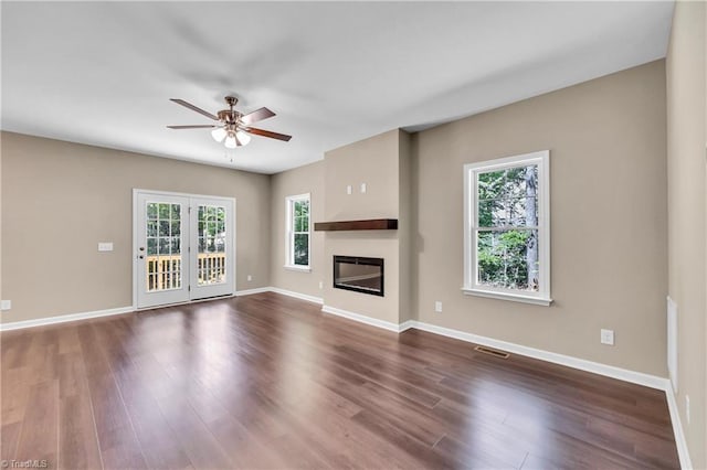 unfurnished living room with a ceiling fan, plenty of natural light, dark wood-style floors, and a glass covered fireplace