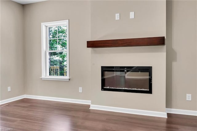 unfurnished living room with a glass covered fireplace, wood finished floors, and baseboards
