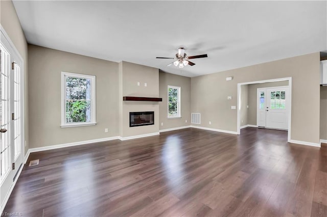 unfurnished living room with plenty of natural light, a ceiling fan, dark wood-style flooring, and a glass covered fireplace