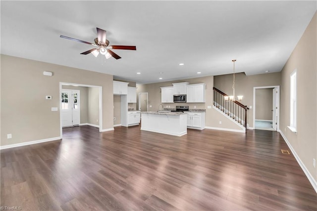 unfurnished living room featuring a sink, a chandelier, stairway, ceiling fan, and baseboards