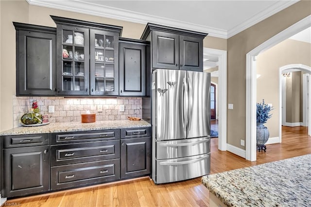 kitchen featuring ornamental molding, decorative backsplash, stainless steel fridge, and light stone countertops