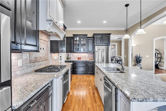 kitchen featuring pendant lighting, sink, appliances with stainless steel finishes, a kitchen island with sink, and ornamental molding