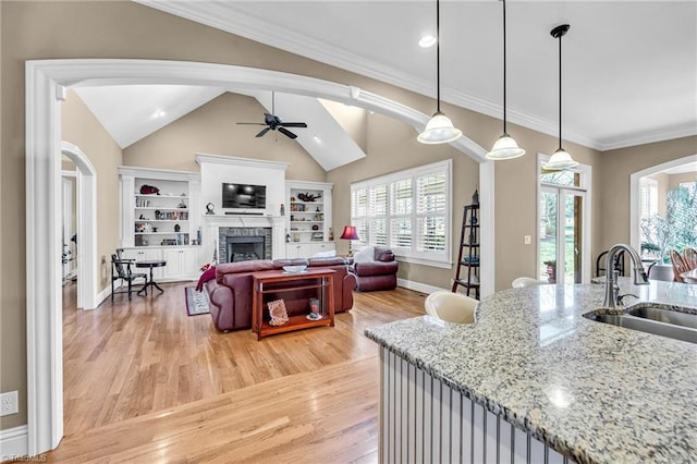 kitchen with sink, ceiling fan, hanging light fixtures, light stone countertops, and light wood-type flooring