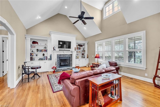 living room with ceiling fan, high vaulted ceiling, a stone fireplace, and light hardwood / wood-style floors