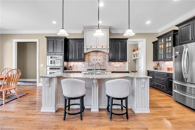 kitchen with a kitchen bar, light hardwood / wood-style flooring, an island with sink, pendant lighting, and stainless steel appliances