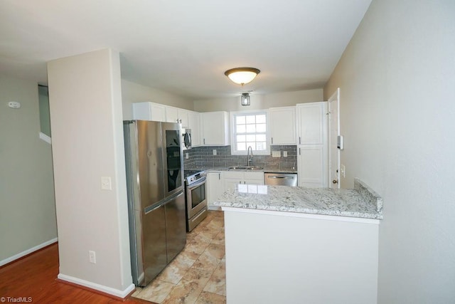 kitchen with sink, white cabinets, decorative backsplash, kitchen peninsula, and stainless steel appliances