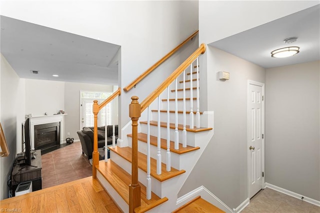 stairway featuring a fireplace with flush hearth, baseboards, tile patterned floors, and visible vents