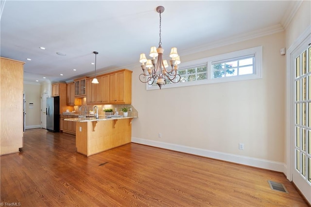 kitchen with a breakfast bar area, stainless steel refrigerator with ice dispenser, baseboards, a peninsula, and ornamental molding