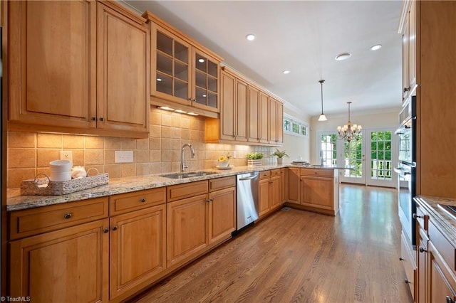 kitchen featuring wood finished floors, dishwasher, a sink, a peninsula, and a notable chandelier