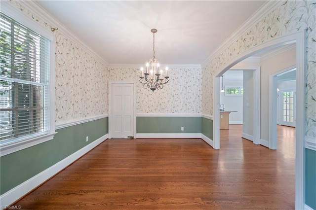 unfurnished dining area with arched walkways, wood finished floors, baseboards, a chandelier, and ornamental molding