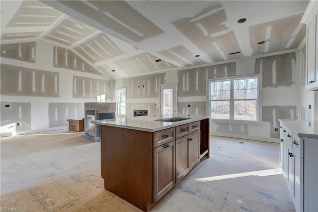 kitchen featuring sink, vaulted ceiling, a fireplace, an island with sink, and white cabinetry