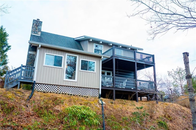 back of property with a wooden deck, a chimney, and roof with shingles