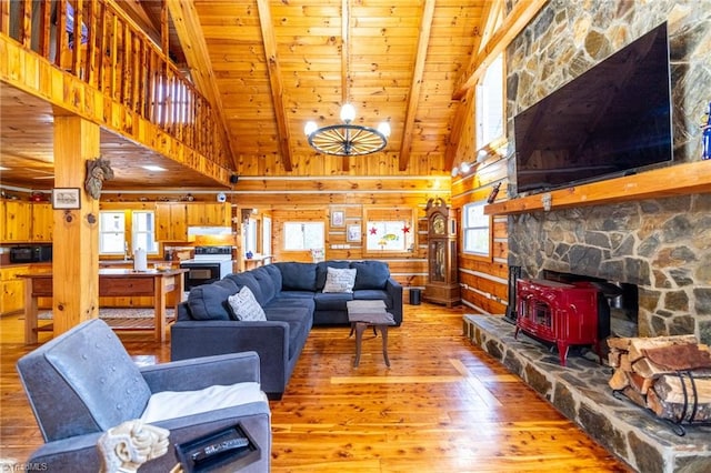 living area featuring a wood stove, beam ceiling, hardwood / wood-style flooring, and a healthy amount of sunlight