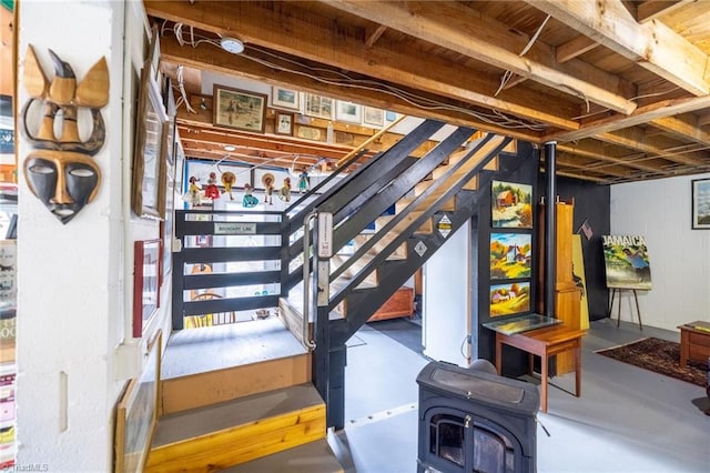 unfinished below grade area featuring concrete block wall, a wood stove, and stairway