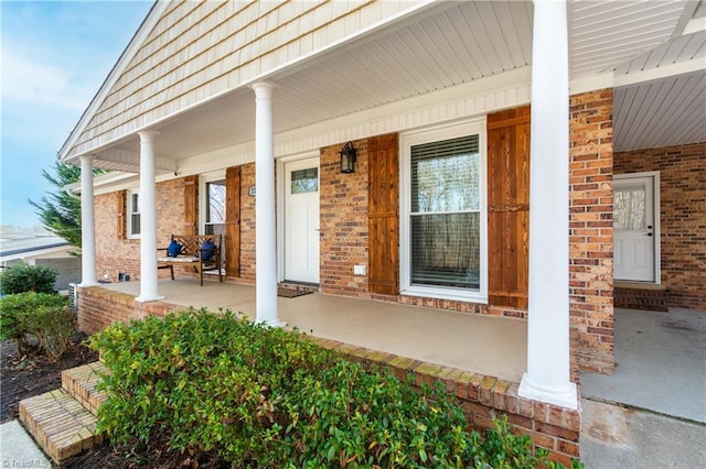 entrance to property featuring a porch and brick siding