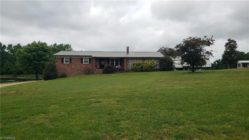 ranch-style home featuring brick siding, a chimney, and a front yard