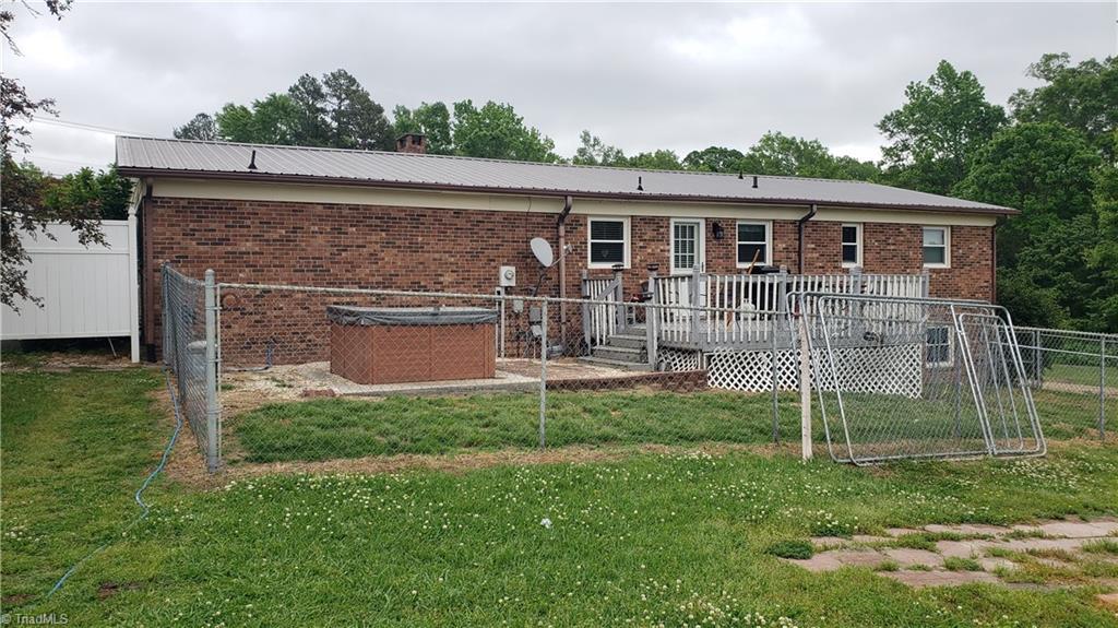 back of house with a lawn, brick siding, fence, and a wooden deck