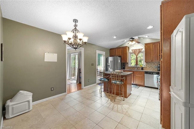 4012 Clarendon Ave, Winston-Salem, NC 27106 - kitchen featuring stainless steel appliances, brown cabinets, plenty of natural light, vaulted ceiling, and backsplash