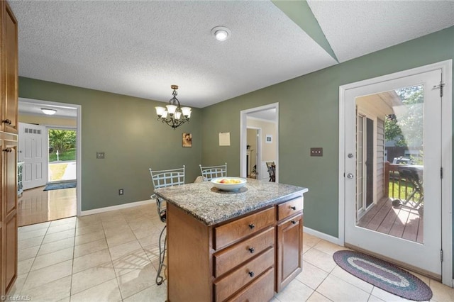 4012 Clarendon Ave, Winston-Salem, NC 27106 - kitchen with light tile patterned floors, a chandelier, brown cabinetry, a kitchen breakfast bar, and a textured ceiling