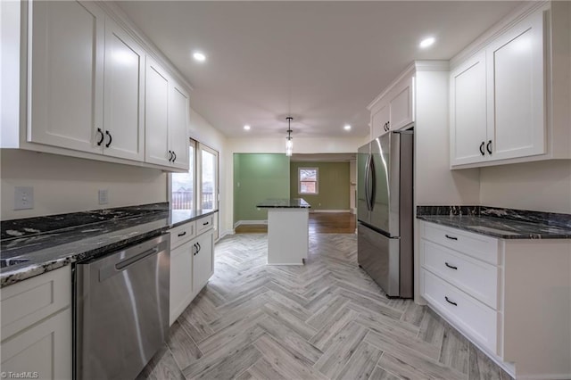 kitchen featuring white cabinets, dark stone counters, appliances with stainless steel finishes, and light parquet floors