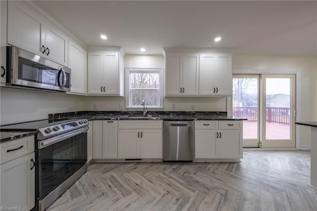 kitchen featuring dark stone counters, stainless steel appliances, sink, light parquet flooring, and white cabinetry