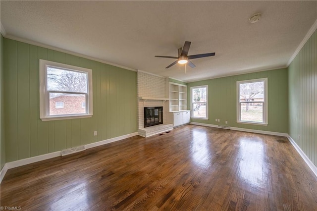 unfurnished living room featuring built in shelves, a brick fireplace, ceiling fan, and crown molding