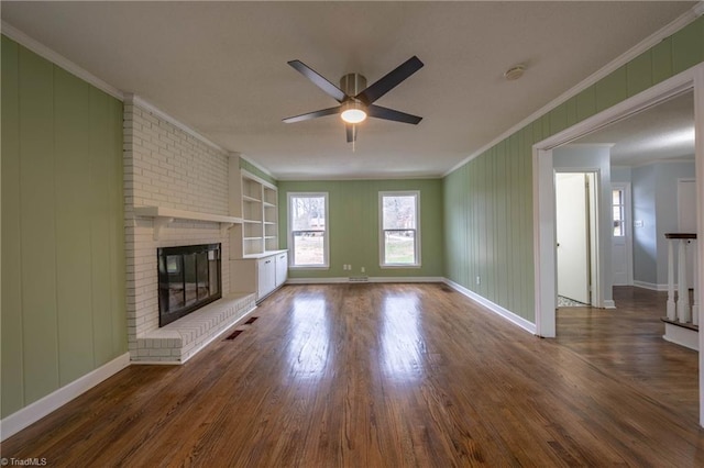 unfurnished living room with ceiling fan, dark wood-type flooring, a brick fireplace, built in features, and crown molding