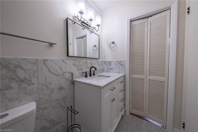 bathroom featuring vanity, toilet, ornamental molding, and tile walls