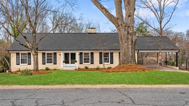 view of front facade with a shingled roof, brick siding, a chimney, and a front lawn