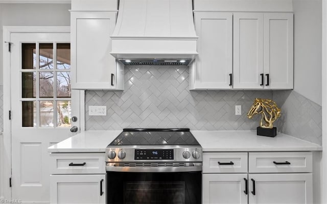 kitchen featuring electric range, white cabinetry, light countertops, decorative backsplash, and custom range hood