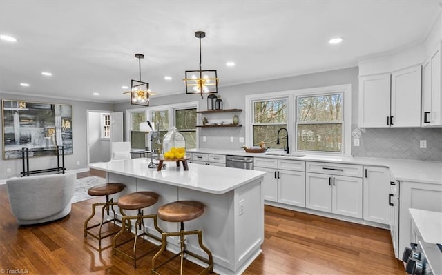 kitchen with a breakfast bar area, light countertops, stainless steel dishwasher, a sink, and hardwood / wood-style flooring