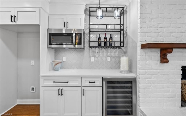 interior space featuring wine cooler, white cabinetry, light countertops, tasteful backsplash, and stainless steel microwave