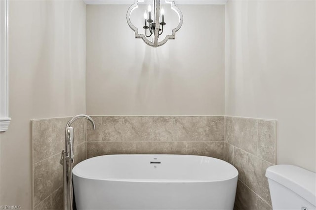 bathroom with a chandelier, a freestanding tub, tile walls, and toilet