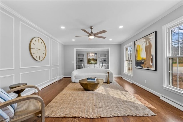 living area with a decorative wall, a baseboard radiator, wood finished floors, and crown molding