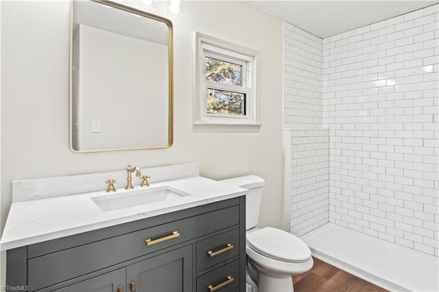 bathroom with toilet, vanity, hardwood / wood-style floors, and tiled shower