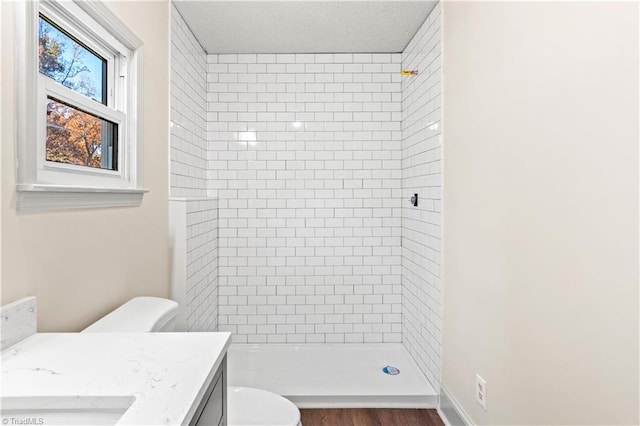 bathroom with tiled shower, vanity, wood-type flooring, and toilet