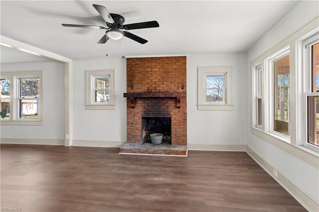 unfurnished living room with a wealth of natural light, a fireplace, ceiling fan, and dark wood-type flooring