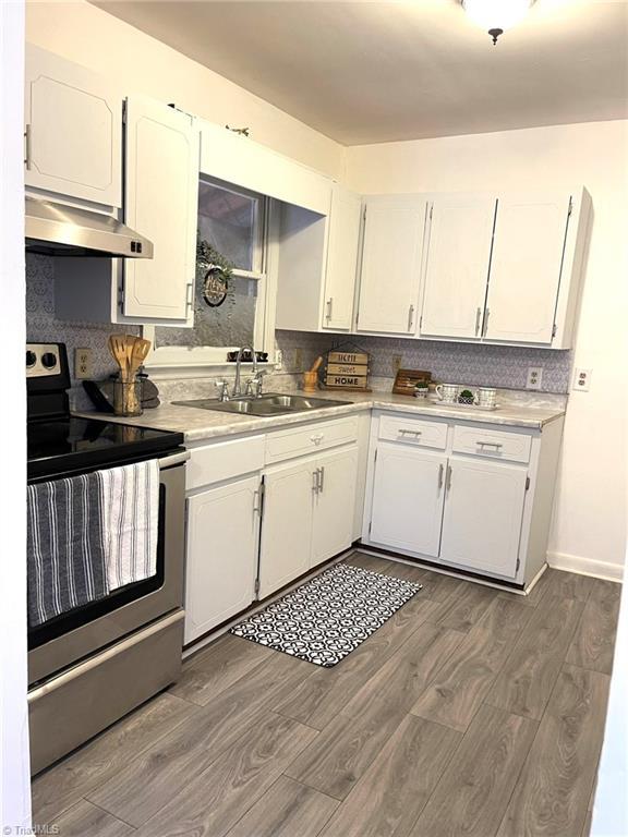 kitchen featuring dark wood-type flooring, stainless steel electric stove, white cabinets, sink, and extractor fan