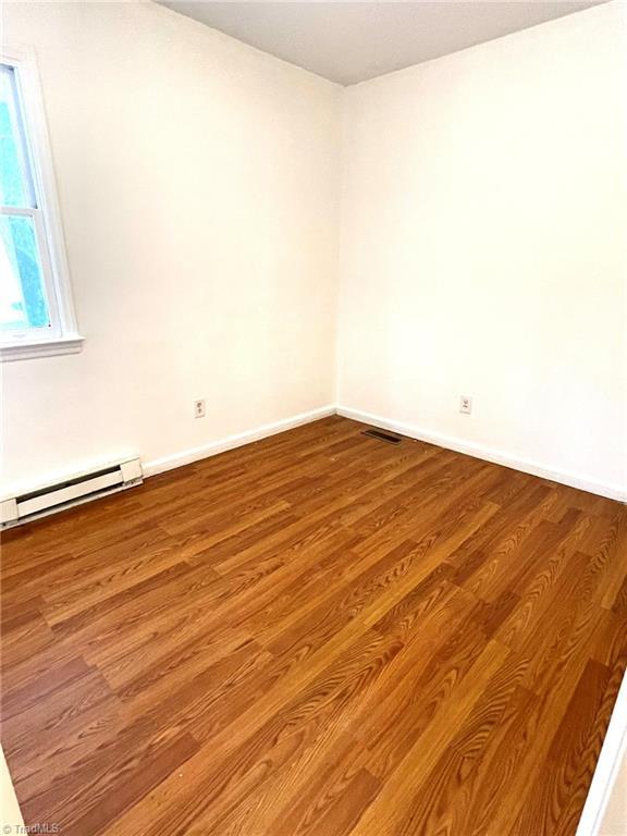 empty room featuring wood-type flooring and a baseboard radiator