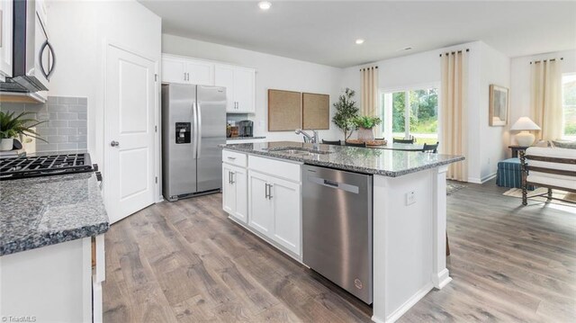 kitchen with stainless steel appliances, wood finished floors, dark stone countertops, and a sink